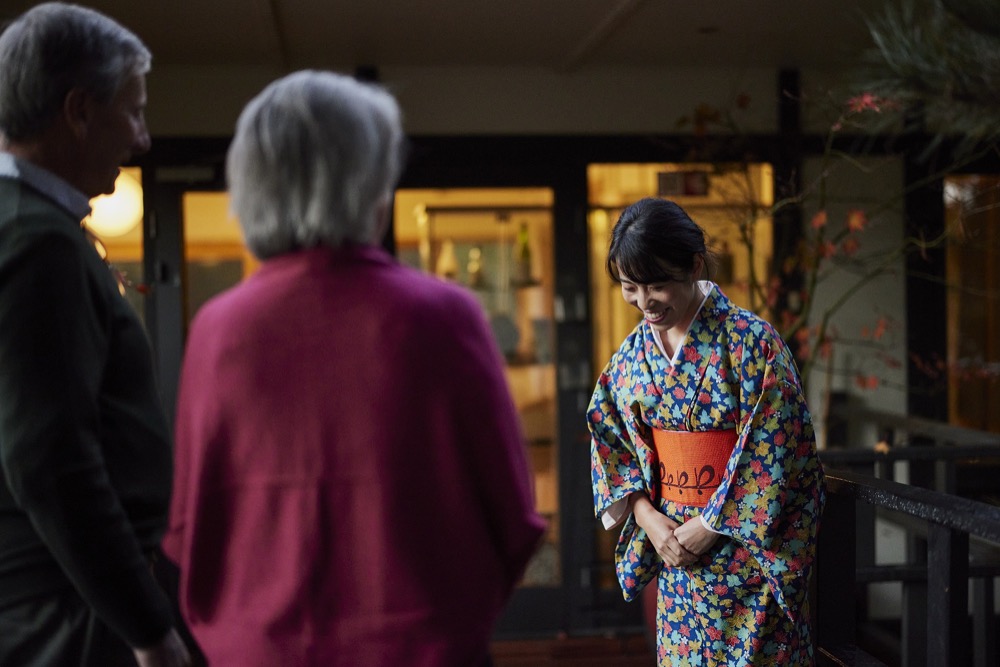 Japanese woman bowing to guests outside restaurant